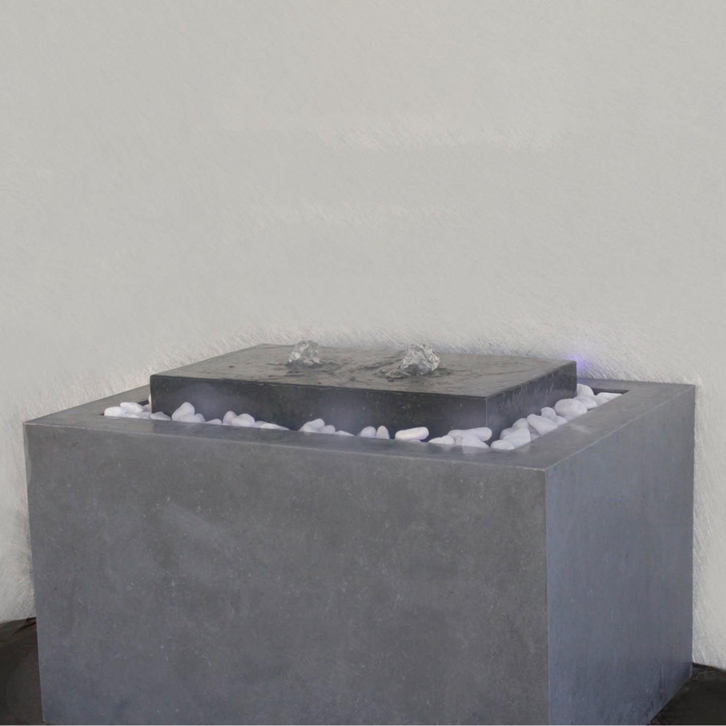 نافورة عصرية مصنوعة من الخرسانة، مزوّدة بفوهة، مع أحجار صغيرة في القاعدة