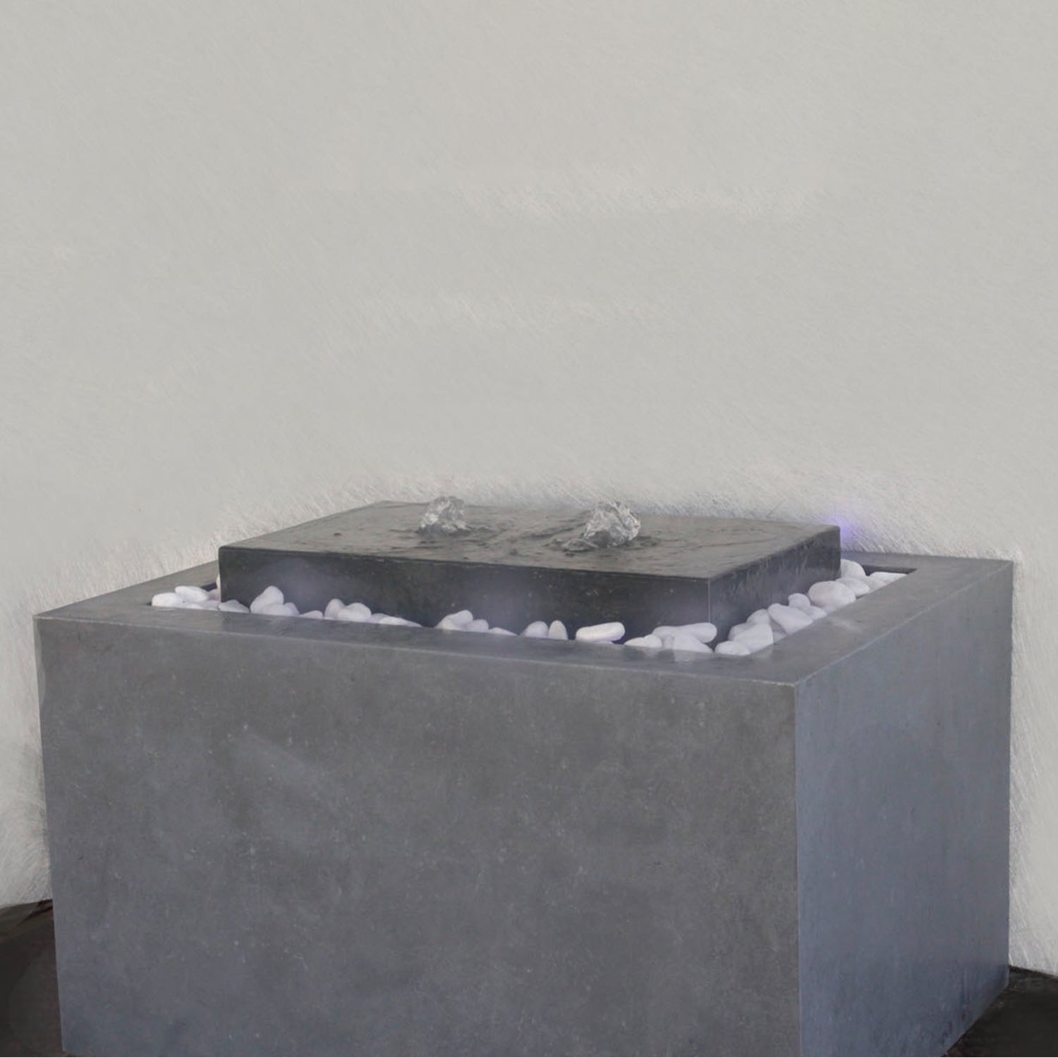 نافورة عصرية مصنوعة من الخرسانة، مزوّدة بفوهة، مع أحجار صغيرة في القاعدة