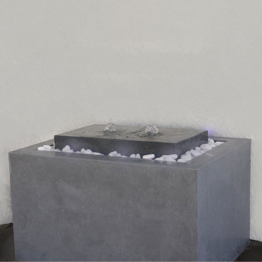 نافورة عصرية مصنوعة من الخرسانة، مزوّدة بفوهة، مع أحجار صغيرة في القاعدة