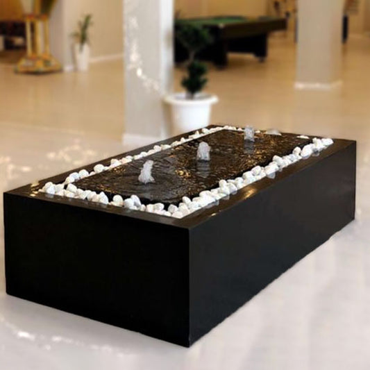 نافورة سوداء مستطيلة بتصميم هندسي يتدفق الماء فيه من الحافة العلوية، موضوعة على أرضية بيضاء لامعة مع أحجار زخرفية حول القاعدة.