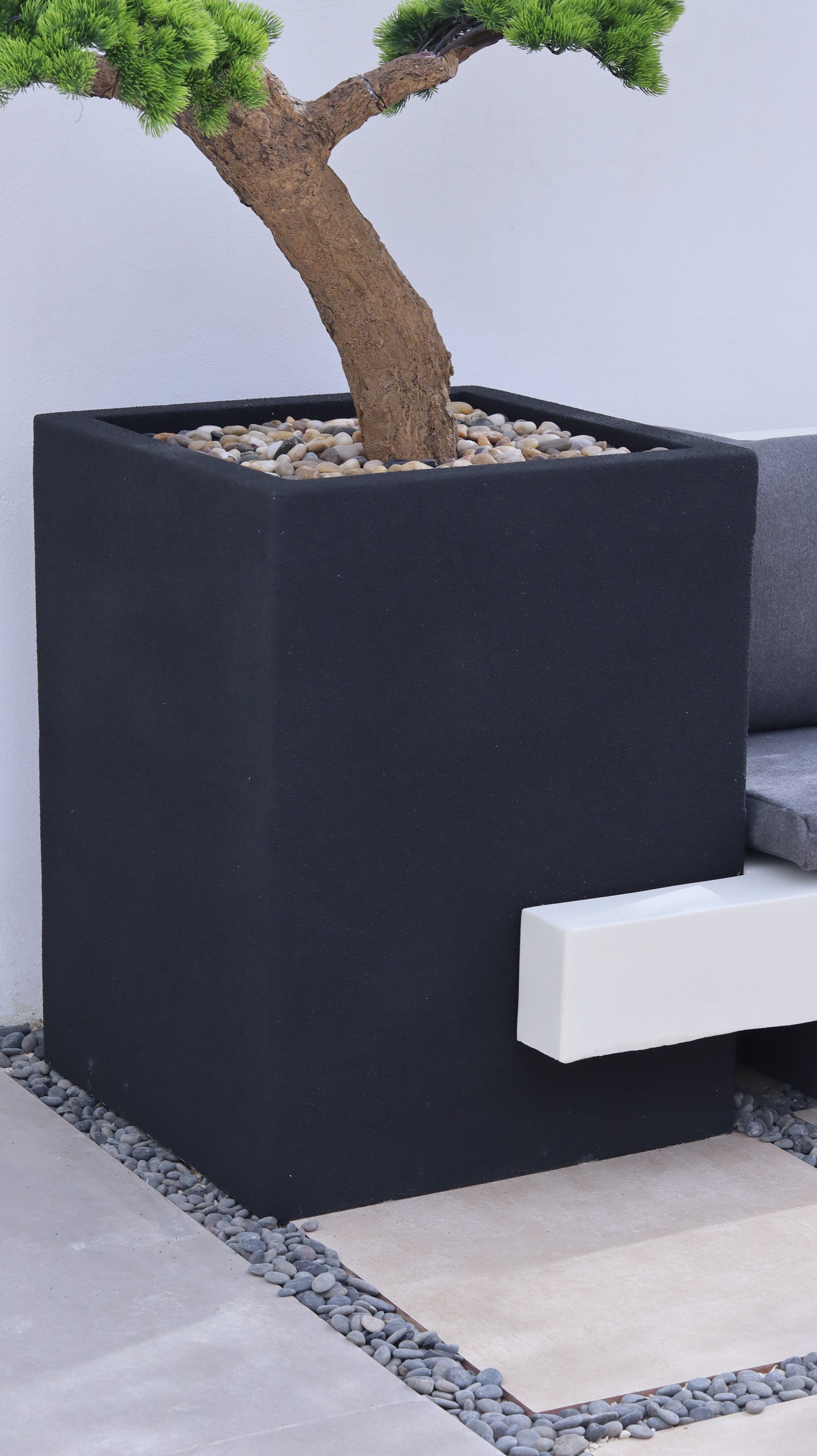 كرسي موري جلسة خارجية بتصميم عصري مع وسائد  ومقعد مدمج بجانب حوض زراعة يحتوي على شجرة بونساي.