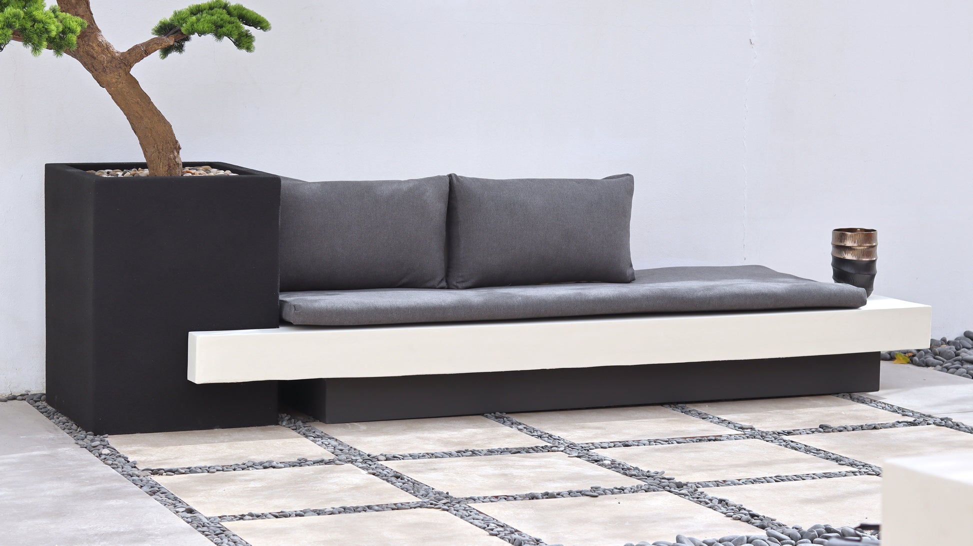 كرسي موري جلسة خارجية بتصميم عصري مع وسائد  ومقعد مدمج بجانب حوض زراعة يحتوي على شجرة بونساي.