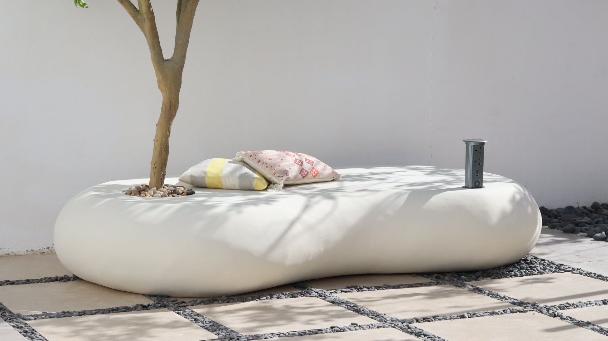 كرسي نيست خارجي  بلون أوف وايت مع شجرة مزروعة ووسائد جلوس، مزود بتوصيلة كهربائية وسماعة مدمجة في فناء حديقة.
